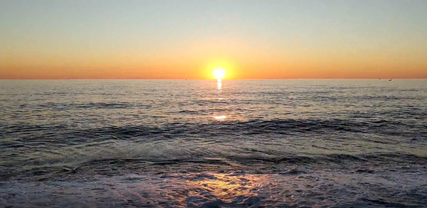 A sunset over the ocean with waves crashing on it.